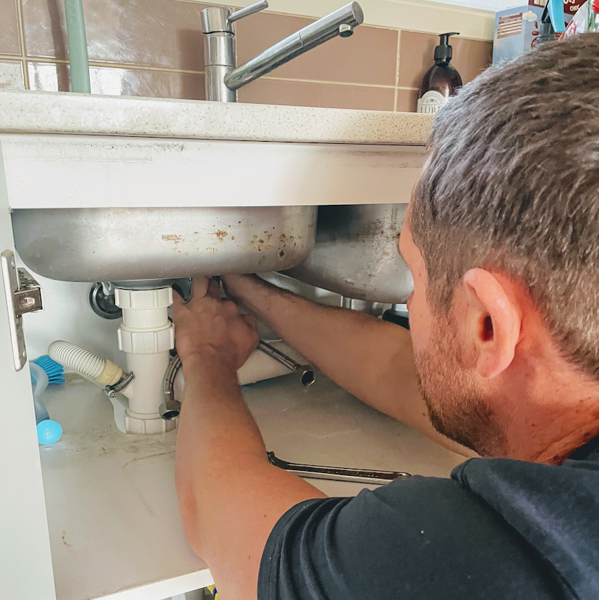 Adam from Norton Plumbing working under a kitchen sink