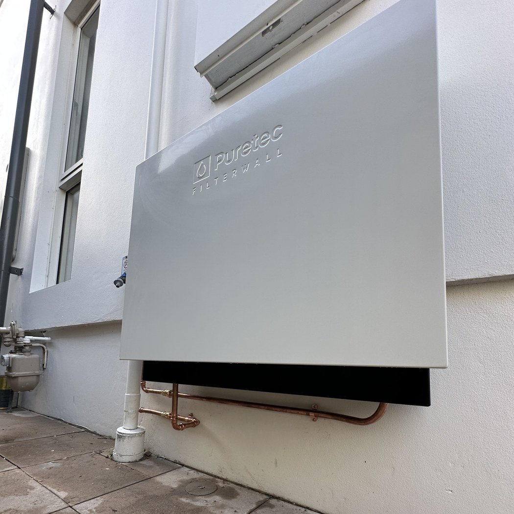 Installed Puretec FilterWall whole-home water filter mounted on the side of a Clovelly home, with copper plumbing visible underneath